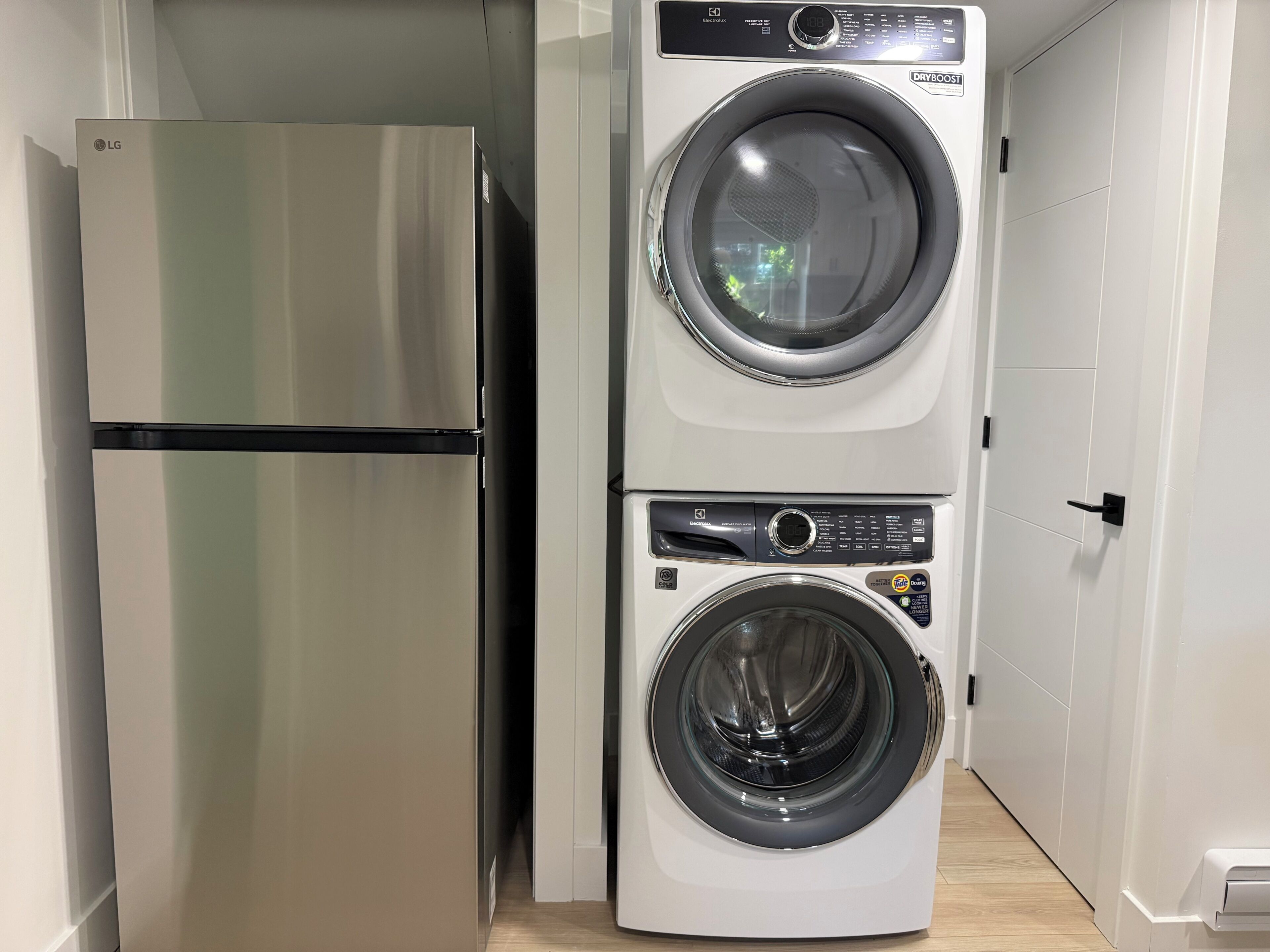 Une cuisine compacte équipée d’un réfrigérateur en acier inoxydable et d’un appareil combiné lave-linge et sèche-linge intégré.