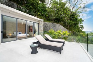 Un moderno espacio lounge al aire libre con dos sillones reclinables y una pequeña mesa, junto a un dormitorio con puerta de vidrio.