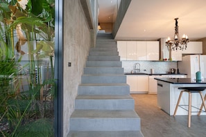 Een moderne keuken met een centraal eiland, een trap naar een hoger gelegen verdieping, en uitzicht op een tuin door een glazen deur.