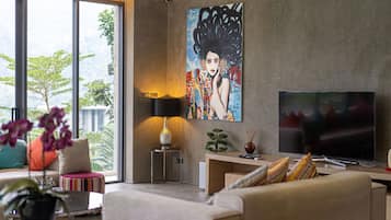 Een moderne woonkamer met een grote televisie, een schilderij aan de muur en uitzicht op het groen.