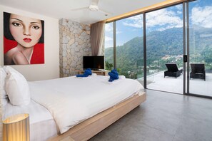 A bedroom with a large bed, a flat-screen TV, a stone wall, and a balcony with a view of the mountains. - Art Deco 3 BR Pool Villa Kamala NP1 (Kathu)