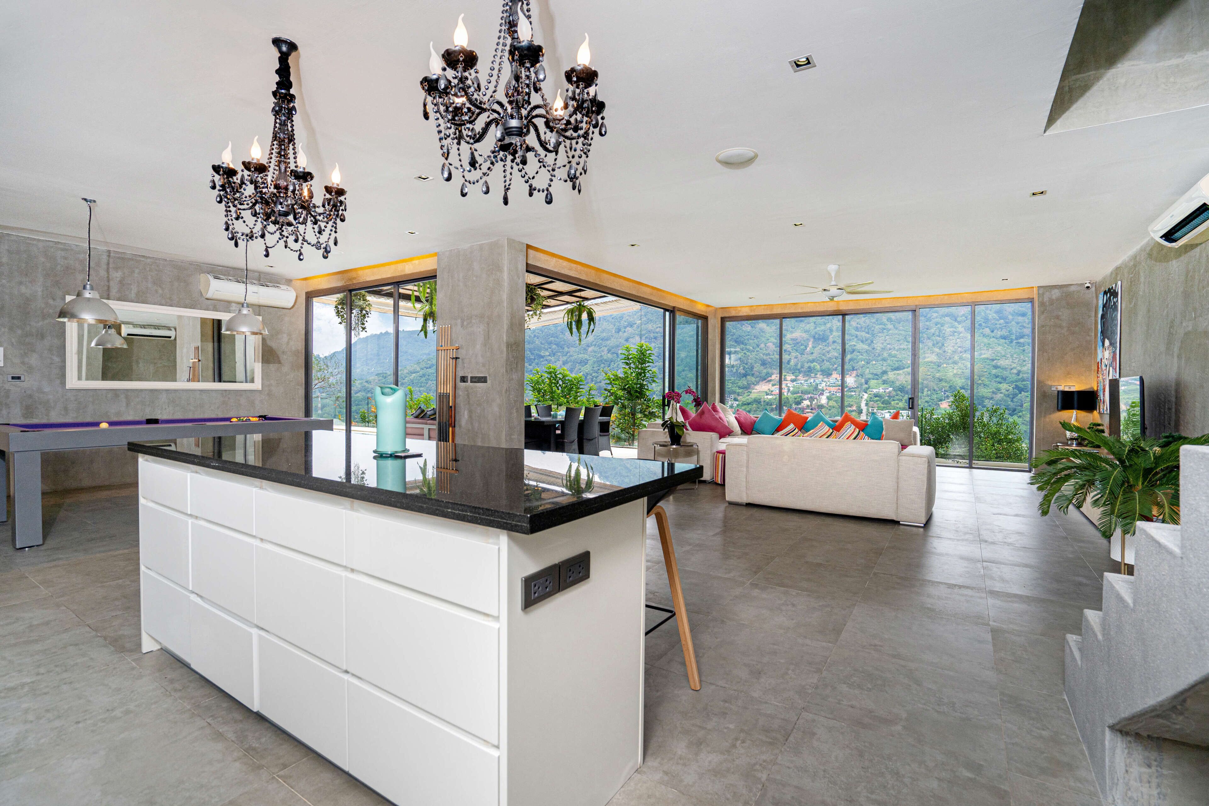 Een moderne keuken met een centraal eiland, een zithoek met een bank en grote ramen met uitzicht op de omgeving.