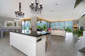 Una cocina moderna con una isla central, un área de comedor con sofá y ventanas amplias que ofrecen vistas al exterior.