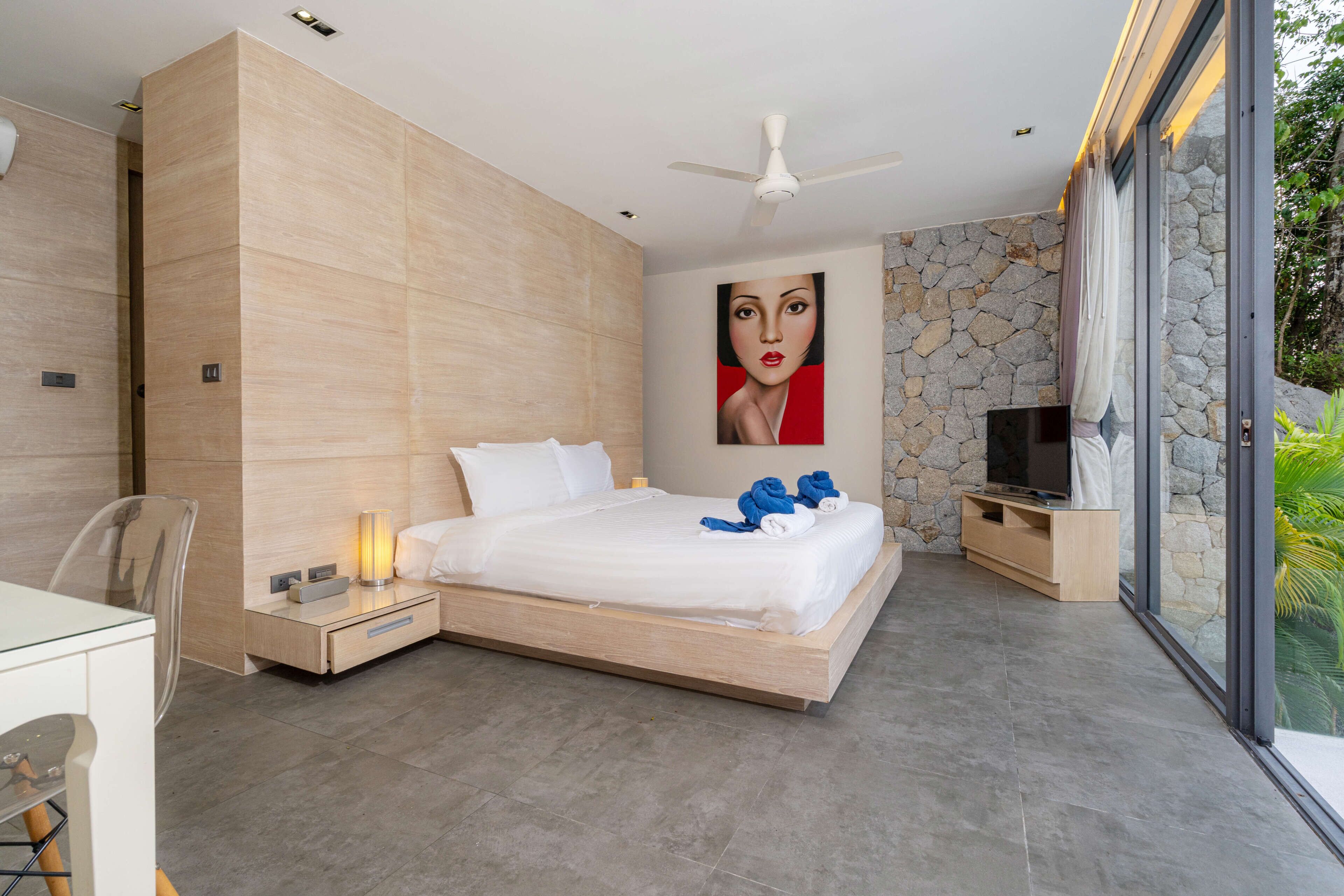 Une chambre moderne avec un grand lit, un ventilateur de plafond, une télévision et un mur en pierre.