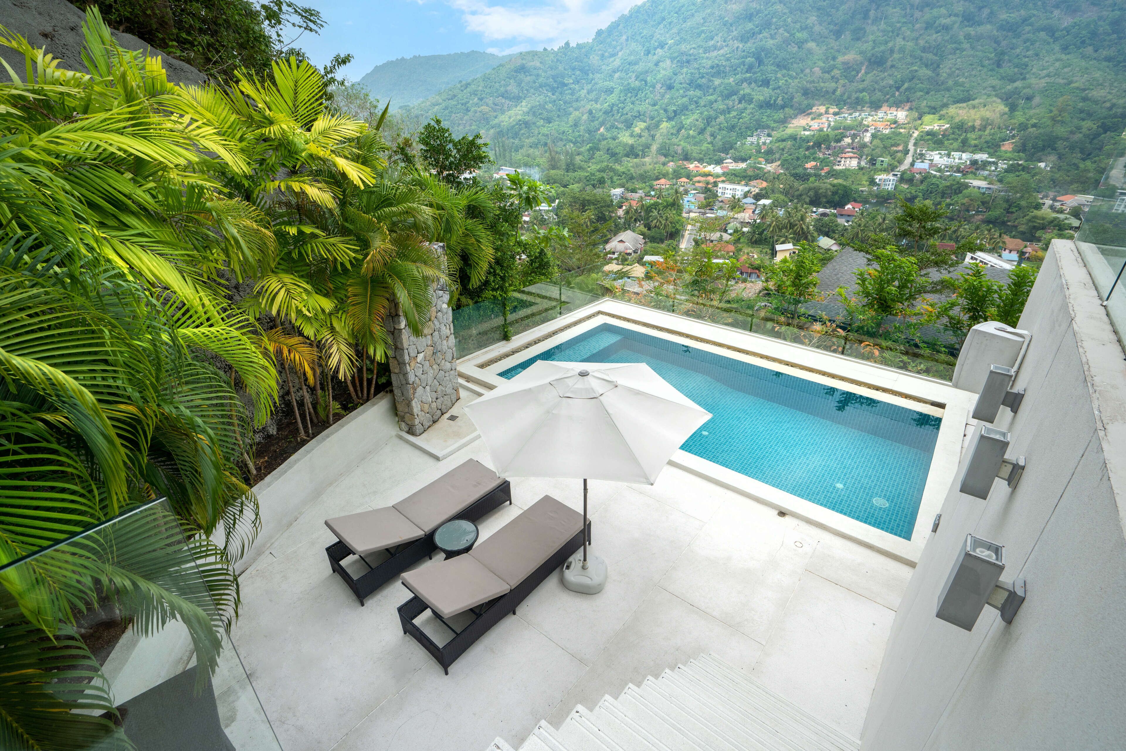 Área de piscina en la azotea con sillones de descanso y una sombrilla, rodeada de exuberante vegetación y vistas a un paisaje montañoso.