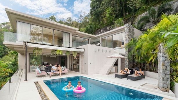 Ett modernt hus med en swimmingpool, utomhusmöbler och frodig grönska.