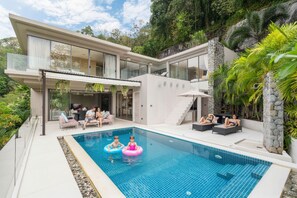 Una casa moderna con piscina, mobiliario exterior y abundante vegetación.
