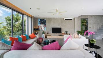 Een moderne woonkamer met een grote bank, kleurrijke kussens, een flatscreen televisie en een plafondventilator.