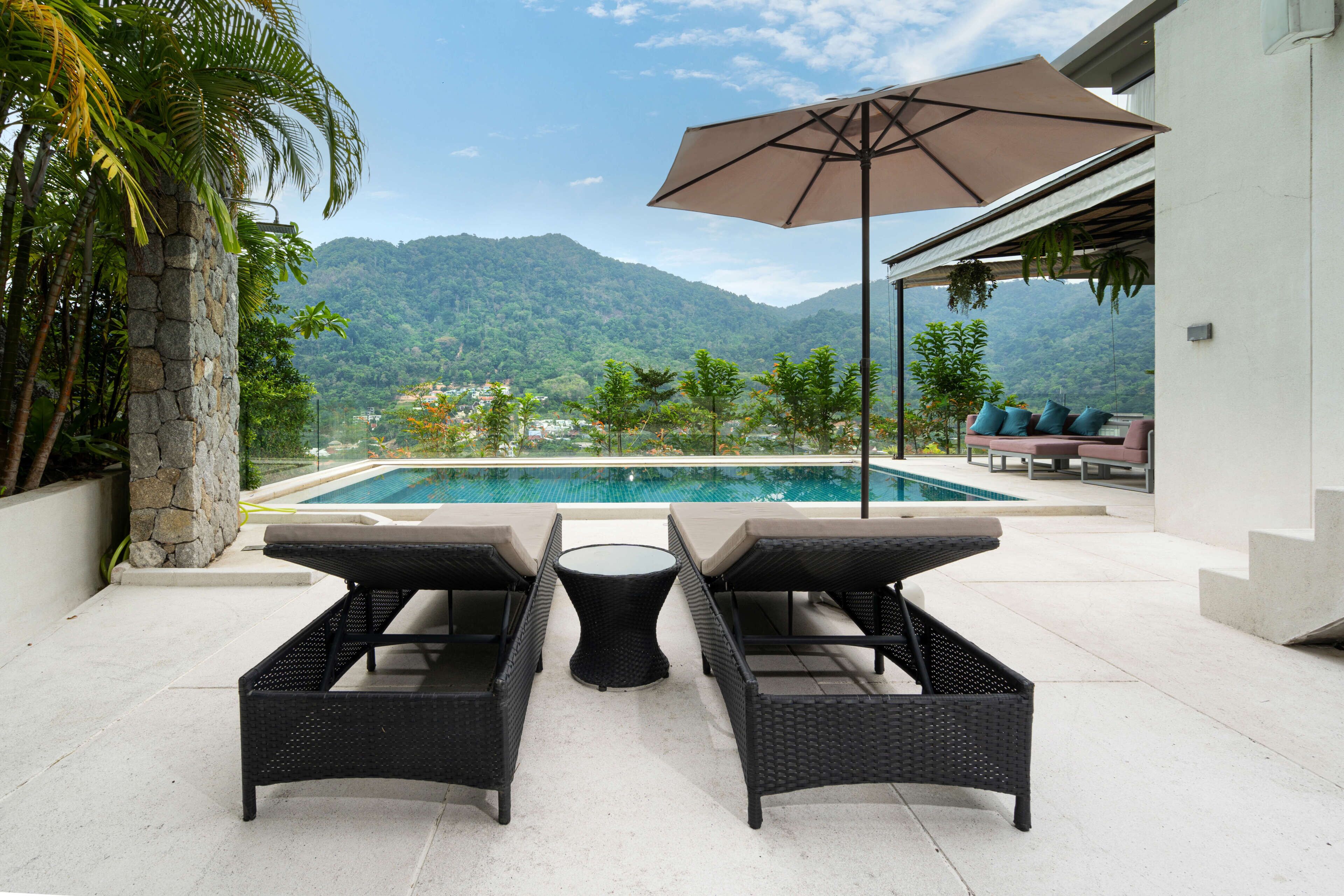 Zona junto a la piscina con dos sillones de mimbre y una mesa, con vistas a una montaña y una piscina.