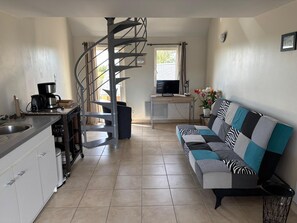 A compact kitchen with a spiral staircase, a sofa with patterned cushions, and a television in the background. - Relaxing Holiday Home in Normandy (Courtils)