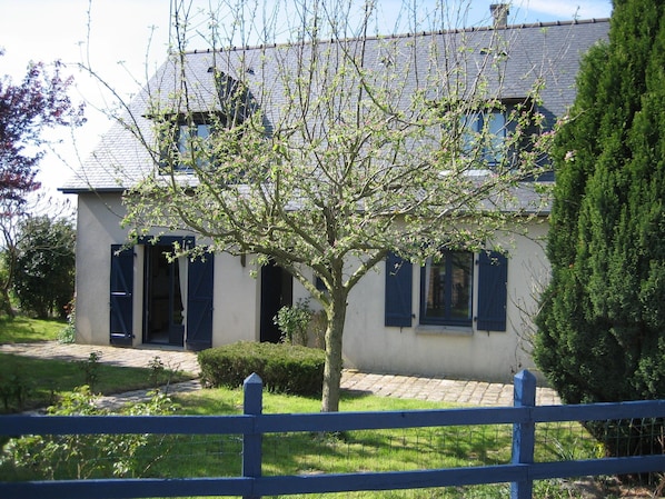 A two-story house with a tree in the front yard, a paved driveway, and a blue fence. - Relaxing Holiday Home in Normandy (Courtils)