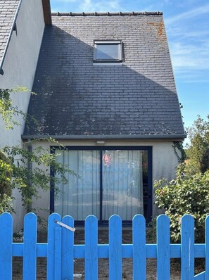 A house with a sloped roof, a small window, and a blue fence in the foreground. - Relaxing Holiday Home in Normandy (Courtils)