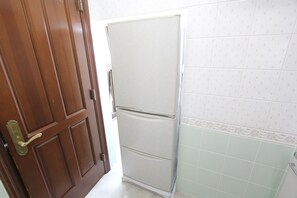 A closed wooden door with a brass handle, a white refrigerator, and patterned wall tiles. - Spacious Private Stay Near Higashi-Shinjuku | Sleeps 6 | Families & Groups | WiFi (3) (新宿区新宿７丁目)