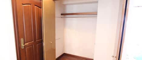 Una habitación con puerta de madera, un armario con barra para colgar ropa y suelo de madera.