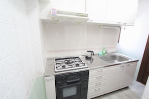 A compact kitchen with a gas stove, an oven, a sink, and a window above the counter. - Spacious Private Stay Near Higashi-Shinjuku | Sleeps 6 | Families & Groups | WiFi (3) (新宿区新宿７丁目)