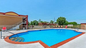 Ein Swimmingpool mit Backsteinbord, eine Treppe, die zu einem Gebäude führt, und ein eingezäunter Bereich mit Liegestühlen.