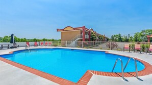 A swimming pool with a red border, surrounded by lounge chairs and a building with a red roof.
