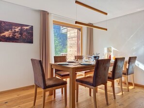 Un coin repas avec une table en bois, six chaises et une vue sur la verdure environnante.