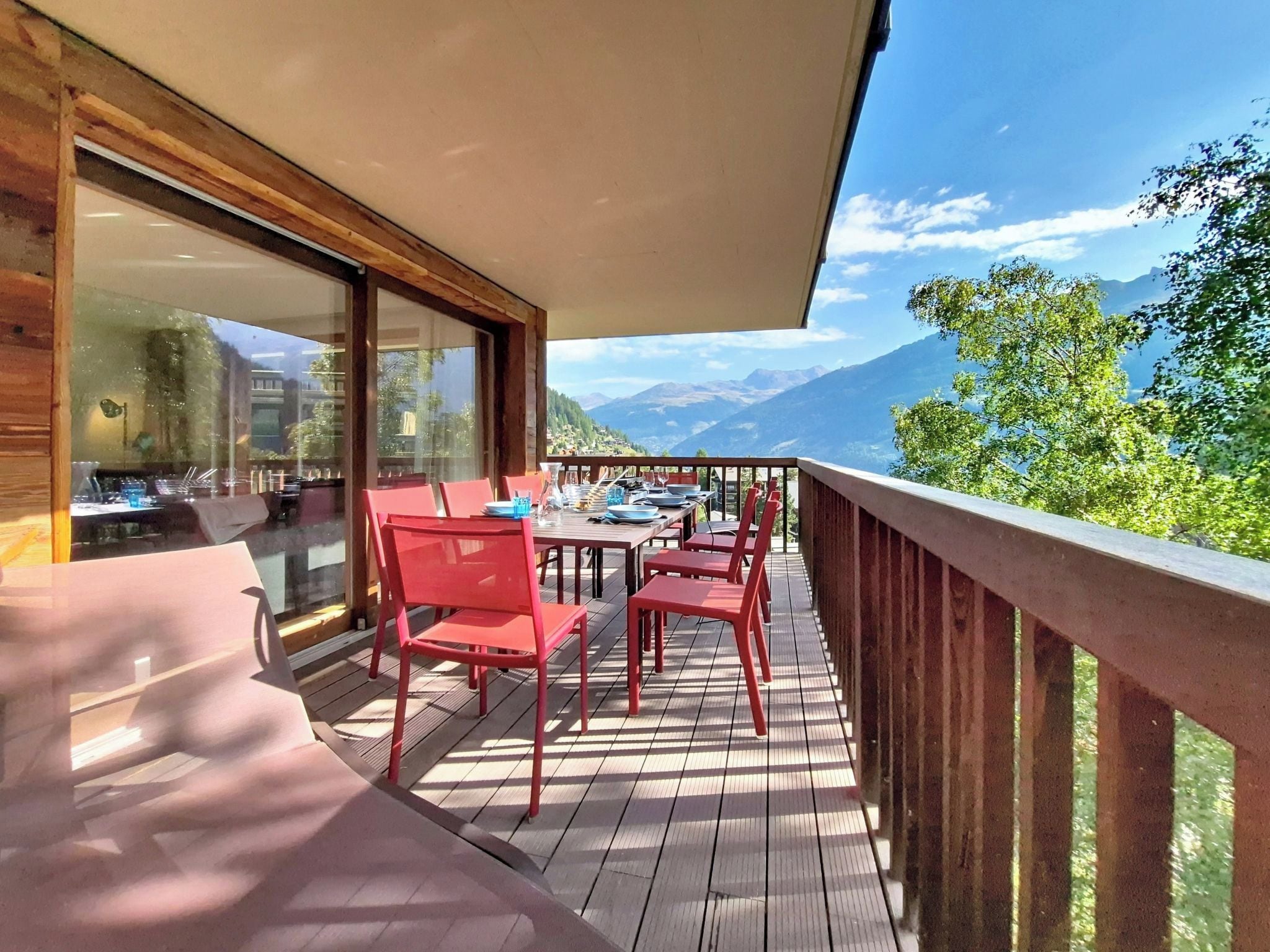A wooden deck with red chairs and tables, overlooking a mountainous landscape.