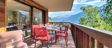 Terraza de madera con sillas y mesas rojas, con vistas a un paisaje montañoso.