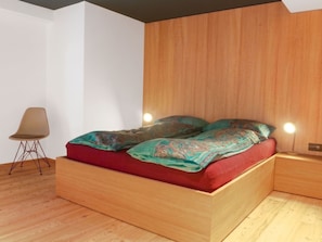 A modern bedroom with a wooden bed frame, a red mattress, and a patterned blanket. - Apartment Armina by Interhome (Zermatt)