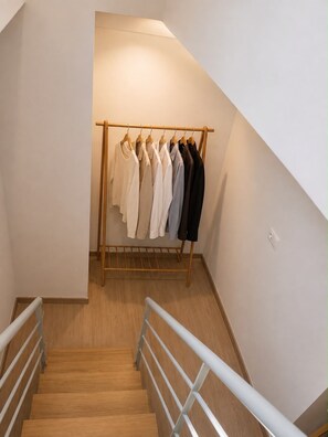 A staircase with a wooden handrail leading to a clothing rack with various garments. - Cozy Maisonette next to Acropolis hill (Athina)
