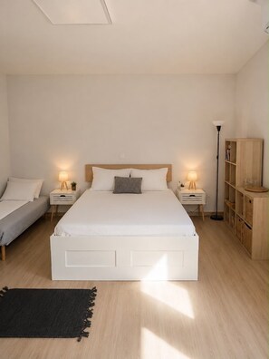A bedroom with a large bed, two bedside tables with lamps, a floor lamp, a wooden cabinet, and a black rug. - Cozy Maisonette next to Acropolis hill (Athina)