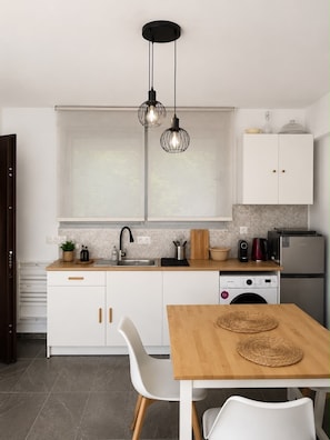 A modern kitchen with white cabinetry, a wooden countertop, a built-in washing machine, and a dining area with a wooden table and chairs. - Cozy Maisonette next to Acropolis hill (Athina)