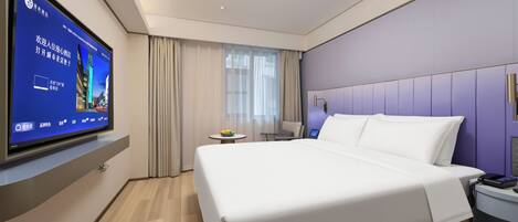 A modern hotel room with a large bed, a flat-screen TV mounted on the wall, a small table with a fruit bowl, and a nightstand with a phone.