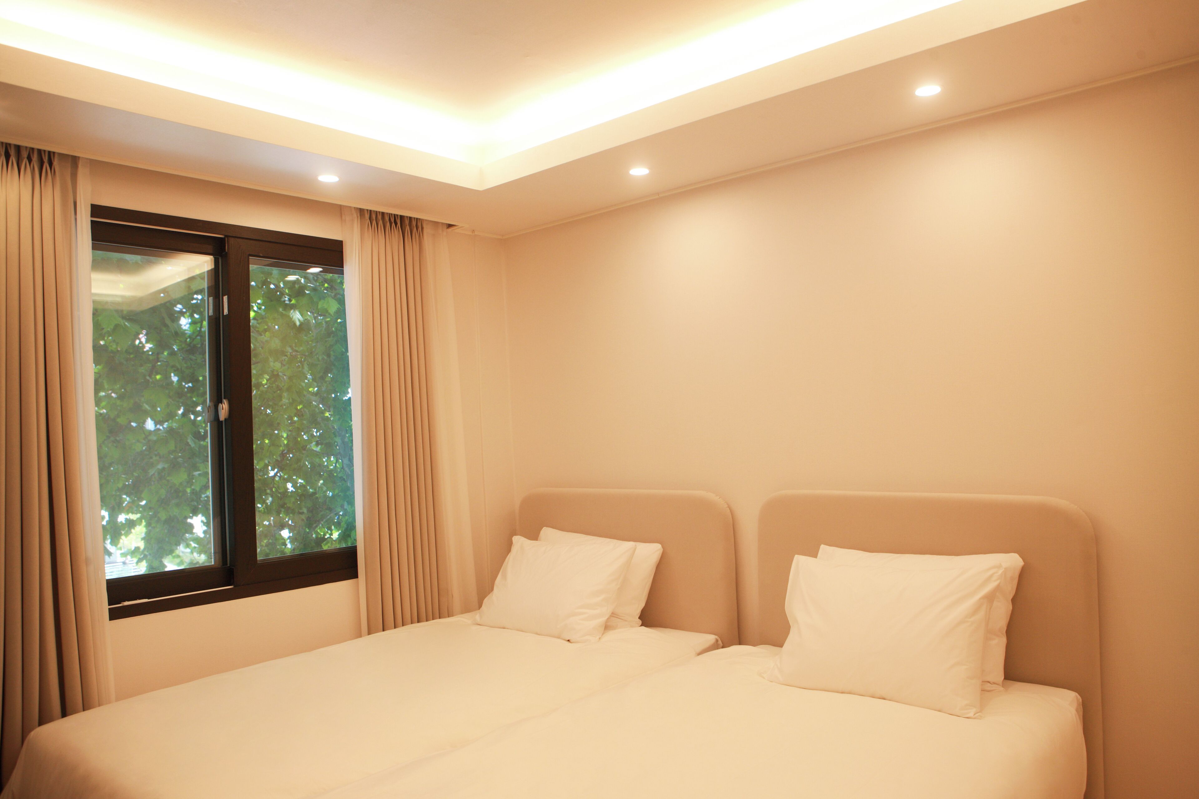 A bedroom with a bed, two pillows, a window with curtains, and recessed ceiling lighting.