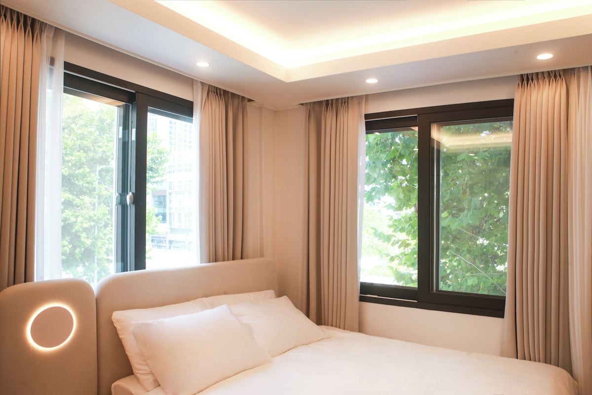 Una habitación de hotel con una cama, una silla y ventanas con cortinas.