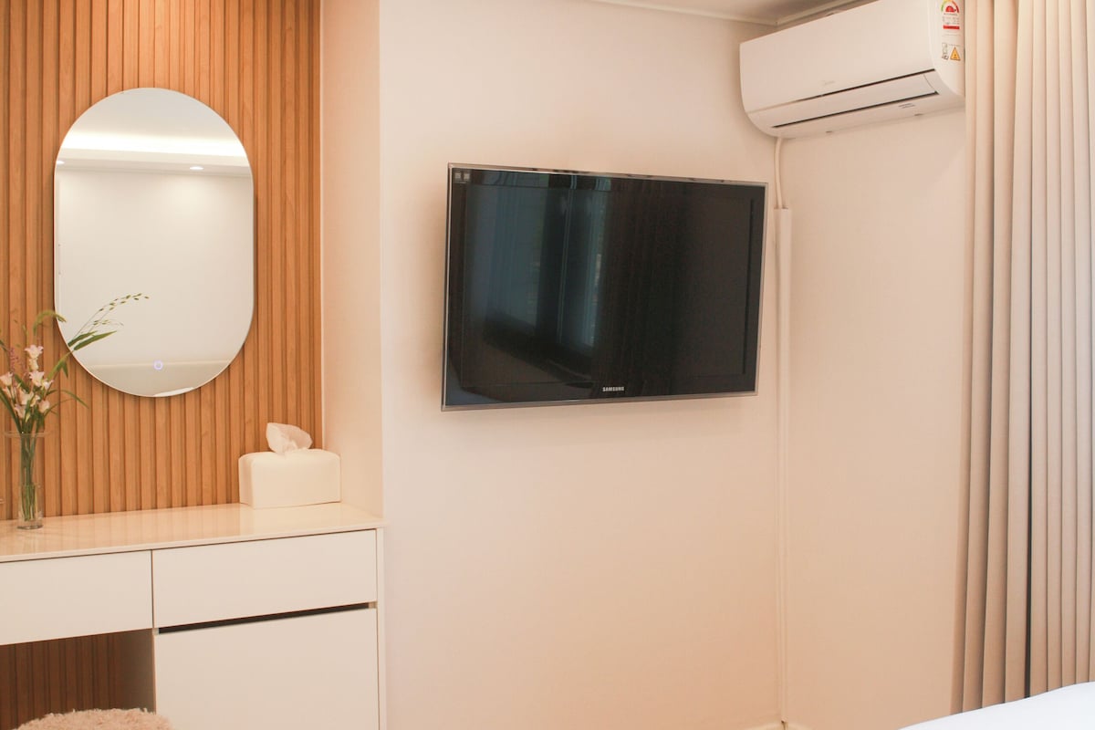 Una habitación de hotel con cama, escritorio con silla, televisor y aire acondicionado.