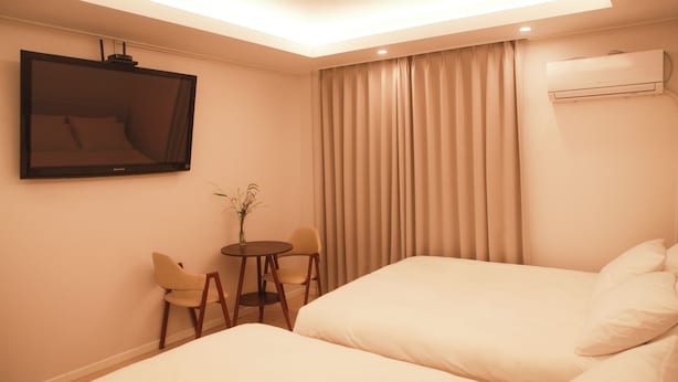 A hotel room with two beds, a TV, a small table with chairs, and a window with curtains. - Olimstay Jamsil (Seoul)