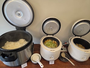Três eletrodomésticos de cozinha com tampas abertas, mostrando arroz e sopa coreana no interior.