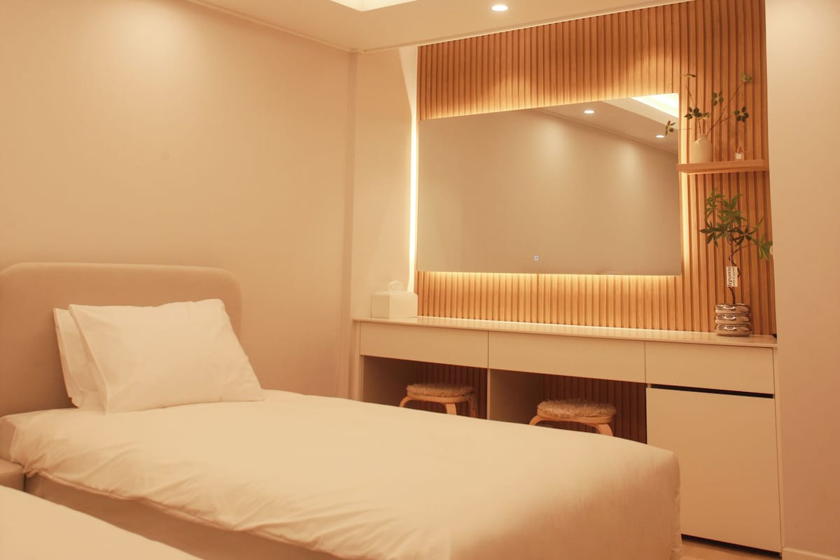 A modern bedroom with a bed, bedside tables, a mirror, and a built-in wooden panel wall.