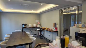 A conference room with a long table, chairs, a coffee station, and a glass partition.