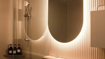 Un baño moderno con un espejo ovalado grande, ducha con mampara de vidrio y lavamanos blanco con un solo grifo.