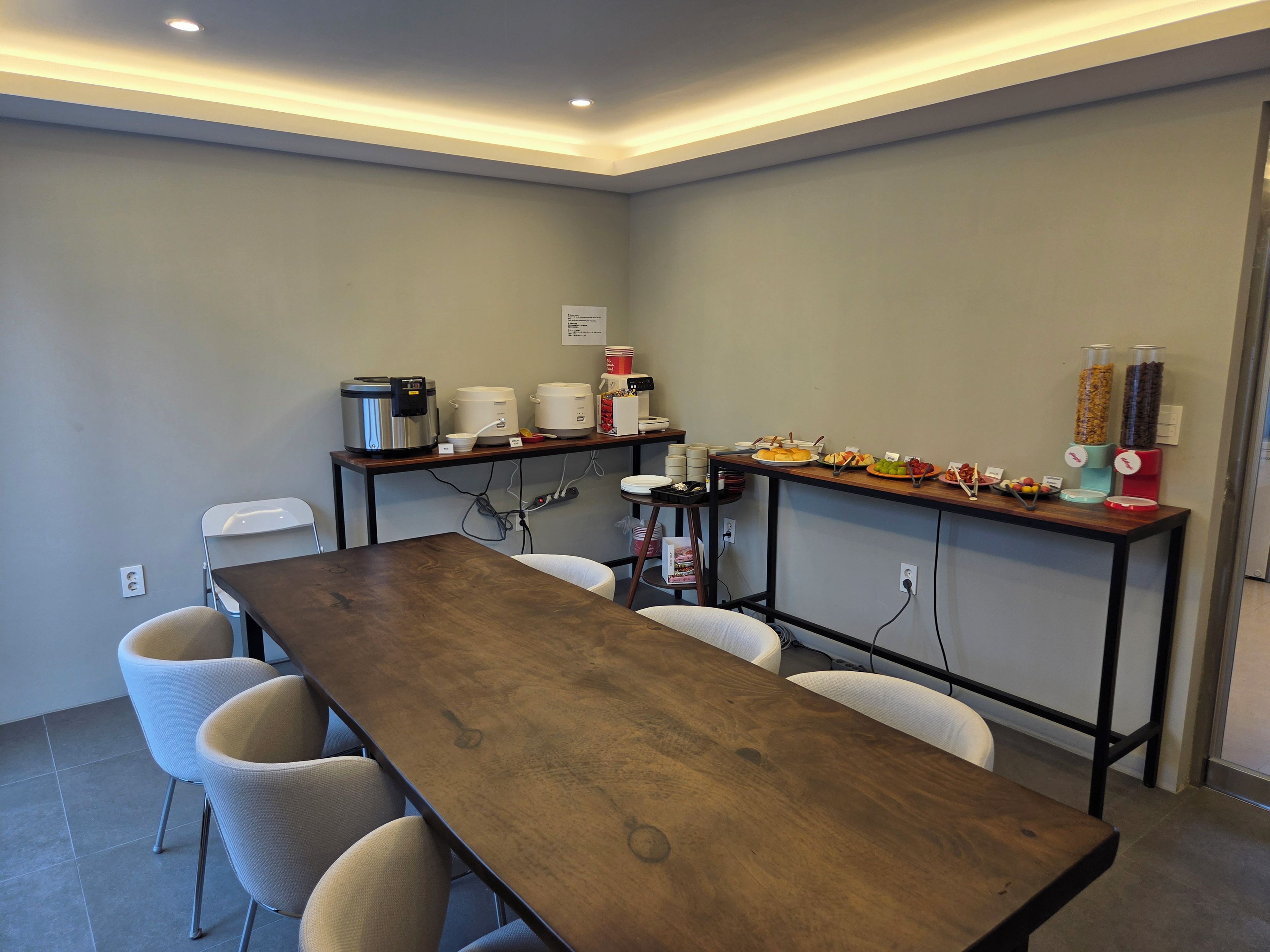A conference room with a long table, white chairs, a buffet table with food and drink dispensers, and a whiteboard on the wall.