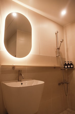 Casa de banho com uma grande pia oval, um espelho, chuveiro com chuveiro manual e prateleira com artigos de higiene pessoal.