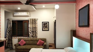 Ein Schlafzimmer mit Bett, Sofa, Deckenventilator, Klimaanlage und einem an der Wand befestigten Fernseher.