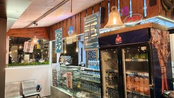 Interior de una cafetería con mostrador, cartel de menú y exhibición de bebidas.