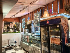 Interior de una cafetería con mostrador, cartel de menú y exhibición de bebidas.