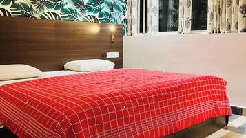 Un dormitorio con pared estampada, cama con colcha roja, ventana con cortinas y cabecera de madera.