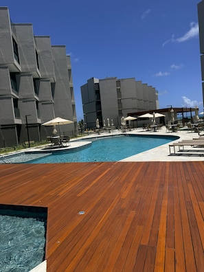 A modern pool area with a wooden deck, lounge chairs, and umbrellas. - Carneiros Beira-Mar | 2Q | Nomar Ecoliving (Tamandare)
