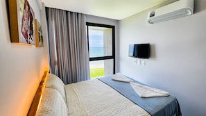 A hotel room with a bed, a TV, a window with curtains, and artwork on the wall. - Carneiros Beira-Mar | 2Q | Nomar Ecoliving (Tamandare)
