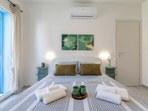 Ein Hotelzimmer mit einem Bett, zwei Nachttischen, einem Vorhangfenster, einer Klimaanlage und zwei Wandgemälden.