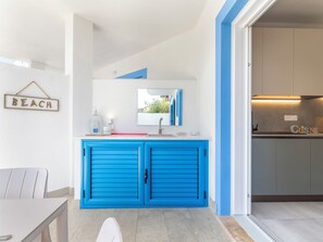 Eine moderne Küche mit blauen Schränken, einer weißen Arbeitsplatte und einem Ausblick ins Freie durch ein Fenster.