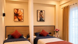 A hotel room with two beds, a bedside table with a vase of flowers, and a large window with curtains. - C Suites Cardiff (Bengaluru)