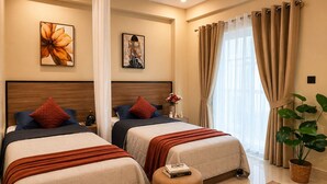 Habitación de hotel con dos camas, un ventanal con cortinas, una planta en maceta y obras de arte en las paredes.
