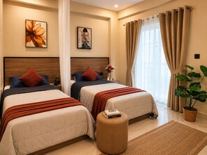 A hotel room with two beds, a large window with curtains, a potted plant, and artwork on the walls. - C Suites Maclean (Bengaluru)